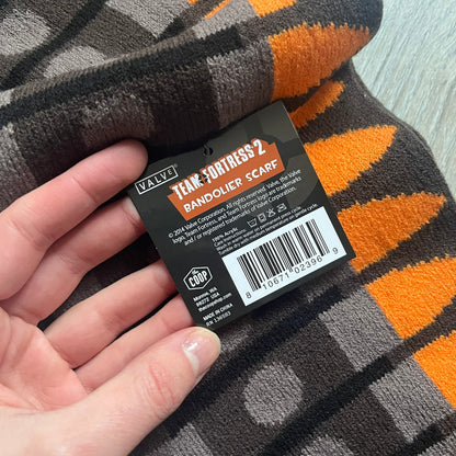 Officially licensed Team Fortress 2 merchandise released in 2014 by The Coop. This scarf is made from soft knit material and features a trompe-l’œil bullet bandolier graphic designed to replicate the ammunition belt worn by the Heavy character. Long and warm in construction, it displays repeated cartridge details along the length of the scarf.