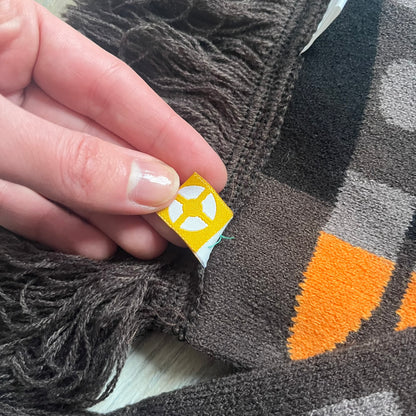 Officially licensed Team Fortress 2 merchandise released in 2014 by The Coop. This scarf is made from soft knit material and features a trompe-l’œil bullet bandolier graphic designed to replicate the ammunition belt worn by the Heavy character. Long and warm in construction, it displays repeated cartridge details along the length of the scarf.