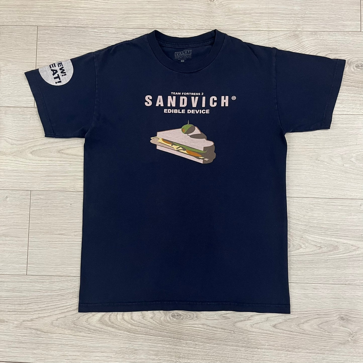 The Team Fortress 2 Sandvich 2010 Tee is an official Valve shirt released in December 2010 and produced during Valve’s in-house merch era. This Navy tee features a Sandvich Edible Device (Heavy secondary weapon) on the front, Sandvich blueprint graphic on the back and 'New Meat!' on the sleeve. A super rare collectible, it represents one of the original Valve Store releases from over a decade ago.