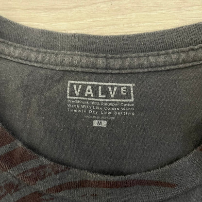 The Team Fortress 2 Spy 2009 Tee is an official Valve shirt from the Sniper vs. Spy update, produced during Valve’s in-house merch era before they switched to a different shirt company. This charcoal tee features a red Spy character holding a butterfly knife and gun, set against a dark red target graphic with dripping effects. A super rare collectible, it represents one of the original Valve Store releases from over a decade ago.