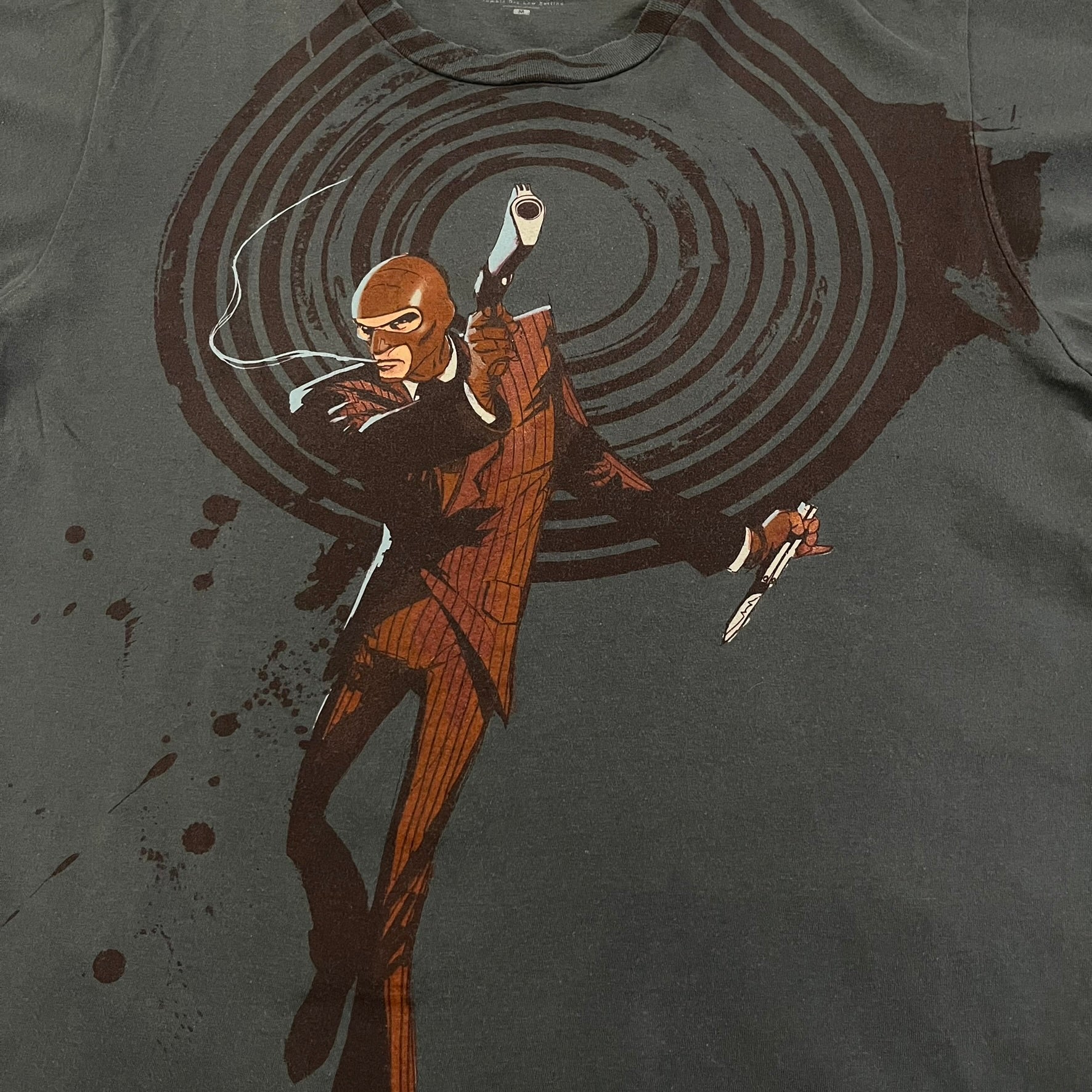 The Team Fortress 2 Spy 2009 Tee is an official Valve shirt from the Sniper vs. Spy update, produced during Valve’s in-house merch era before they switched to a different shirt company. This charcoal tee features a red Spy character holding a butterfly knife and gun, set against a dark red target graphic with dripping effects. A super rare collectible, it represents one of the original Valve Store releases from over a decade ago.