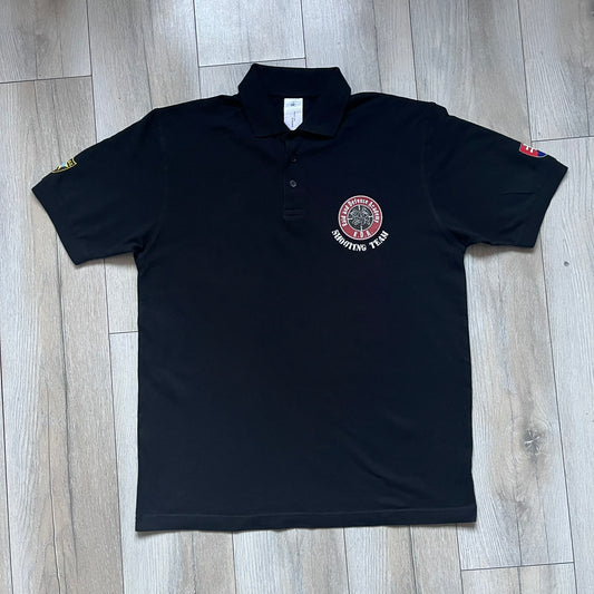 Black polo shirt featuring a large Team Glock logo in white and red printed across the upper back. The chest is marked with the Raid and Defense Academy Shooting Team logo, while the sleeves carry a Slovakia flag badge on one side and an International Practical Shooting Confederation (IPSC) patch on the other. Standard short-sleeve polo construction with a clean, functional finish.