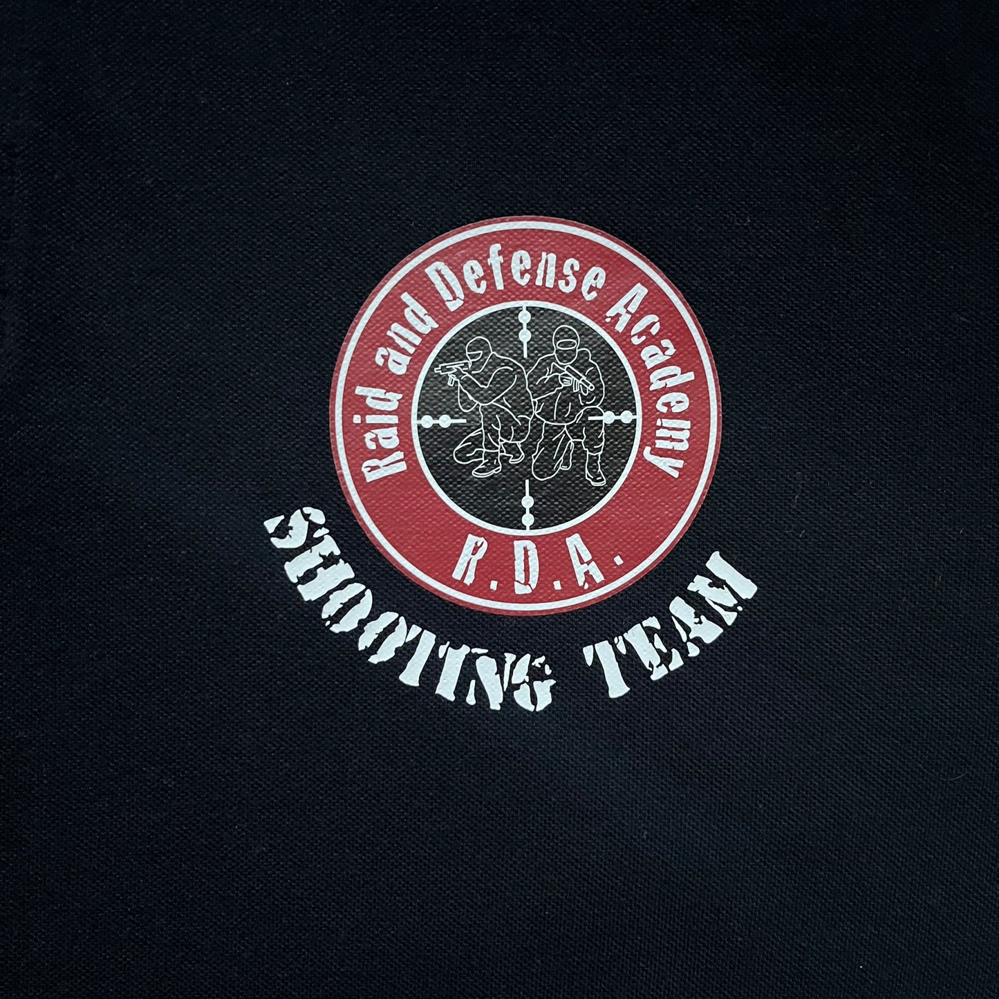 Black polo shirt featuring a large Team Glock logo in white and red printed across the upper back. The chest is marked with the Raid and Defense Academy Shooting Team logo, while the sleeves carry a Slovakia flag badge on one side and an International Practical Shooting Confederation (IPSC) patch on the other. Standard short-sleeve polo construction with a clean, functional finish.