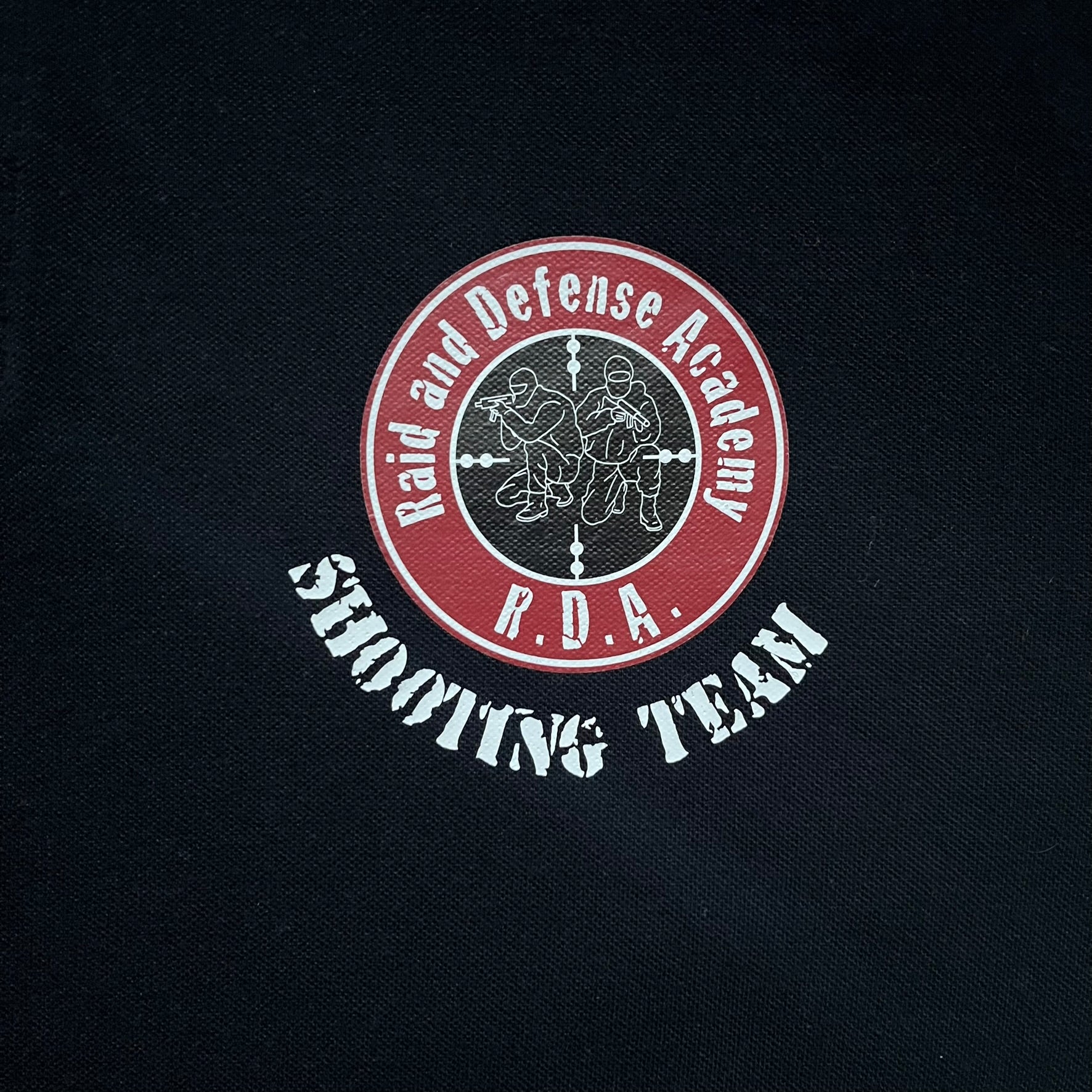 Black polo shirt featuring a large Team Glock logo in white and red printed across the upper back. The chest is marked with the Raid and Defense Academy Shooting Team logo, while the sleeves carry a Slovakia flag badge on one side and an International Practical Shooting Confederation (IPSC) patch on the other. Standard short-sleeve polo construction with a clean, functional finish.