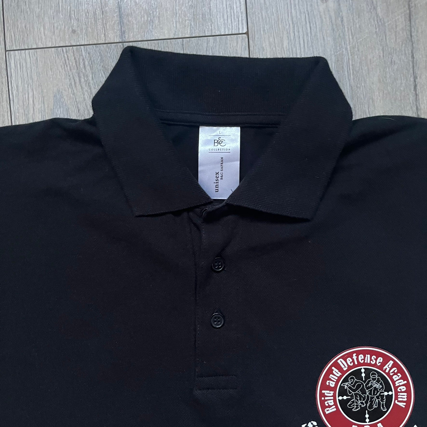 Black polo shirt featuring a large Team Glock logo in white and red printed across the upper back. The chest is marked with the Raid and Defense Academy Shooting Team logo, while the sleeves carry a Slovakia flag badge on one side and an International Practical Shooting Confederation (IPSC) patch on the other. Standard short-sleeve polo construction with a clean, functional finish.