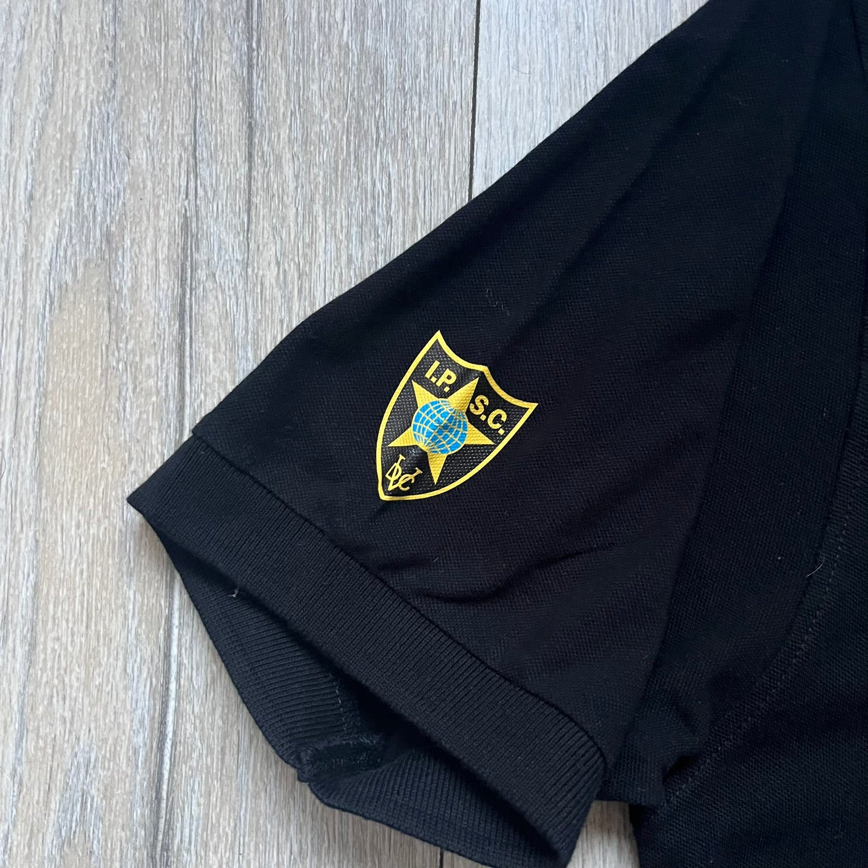 Black polo shirt featuring a large Team Glock logo in white and red printed across the upper back. The chest is marked with the Raid and Defense Academy Shooting Team logo, while the sleeves carry a Slovakia flag badge on one side and an International Practical Shooting Confederation (IPSC) patch on the other. Standard short-sleeve polo construction with a clean, functional finish.