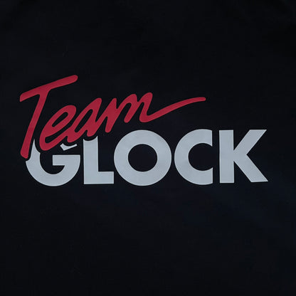 Black polo shirt featuring a large Team Glock logo in white and red printed across the upper back. The chest is marked with the Raid and Defense Academy Shooting Team logo, while the sleeves carry a Slovakia flag badge on one side and an International Practical Shooting Confederation (IPSC) patch on the other. Standard short-sleeve polo construction with a clean, functional finish.