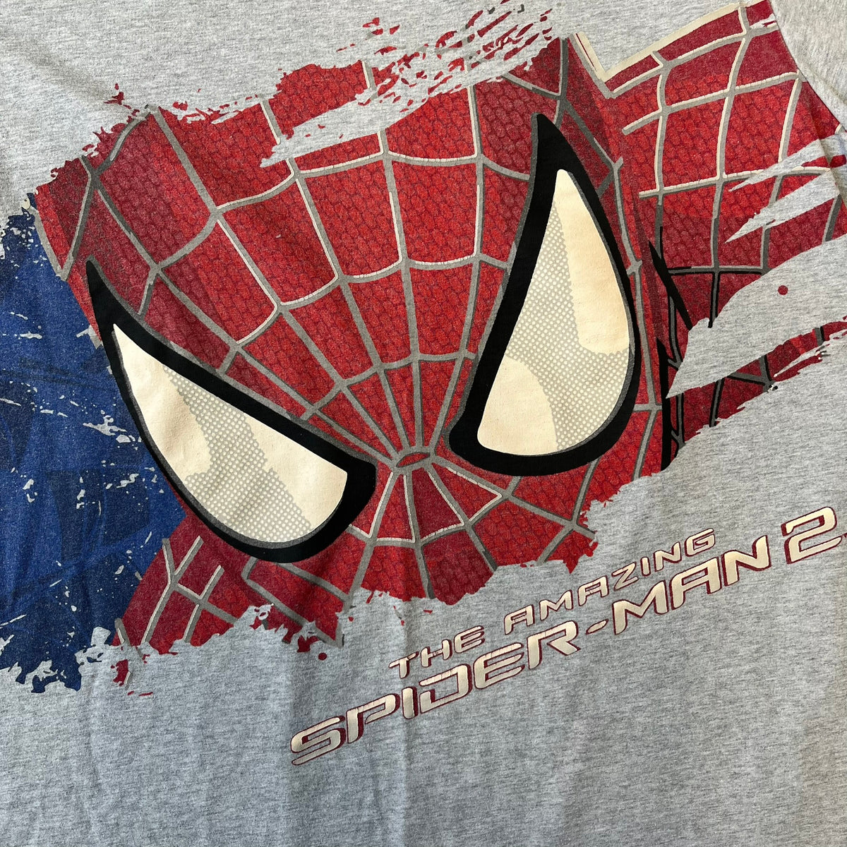 Gray 2014 Marvel tee featuring The Amazing Spider-Man 2 design with a “ripped page” effect showcasing Spider-Man’s face in the center. Text logo sits beneath the graphic for a bold cinematic touch. A collectible piece from the official movie merchandise line.