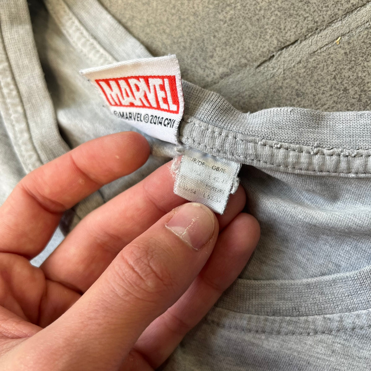 Gray 2014 Marvel tee featuring The Amazing Spider-Man 2 design with a “ripped page” effect showcasing Spider-Man’s face in the center. Text logo sits beneath the graphic for a bold cinematic touch. A collectible piece from the official movie merchandise line.