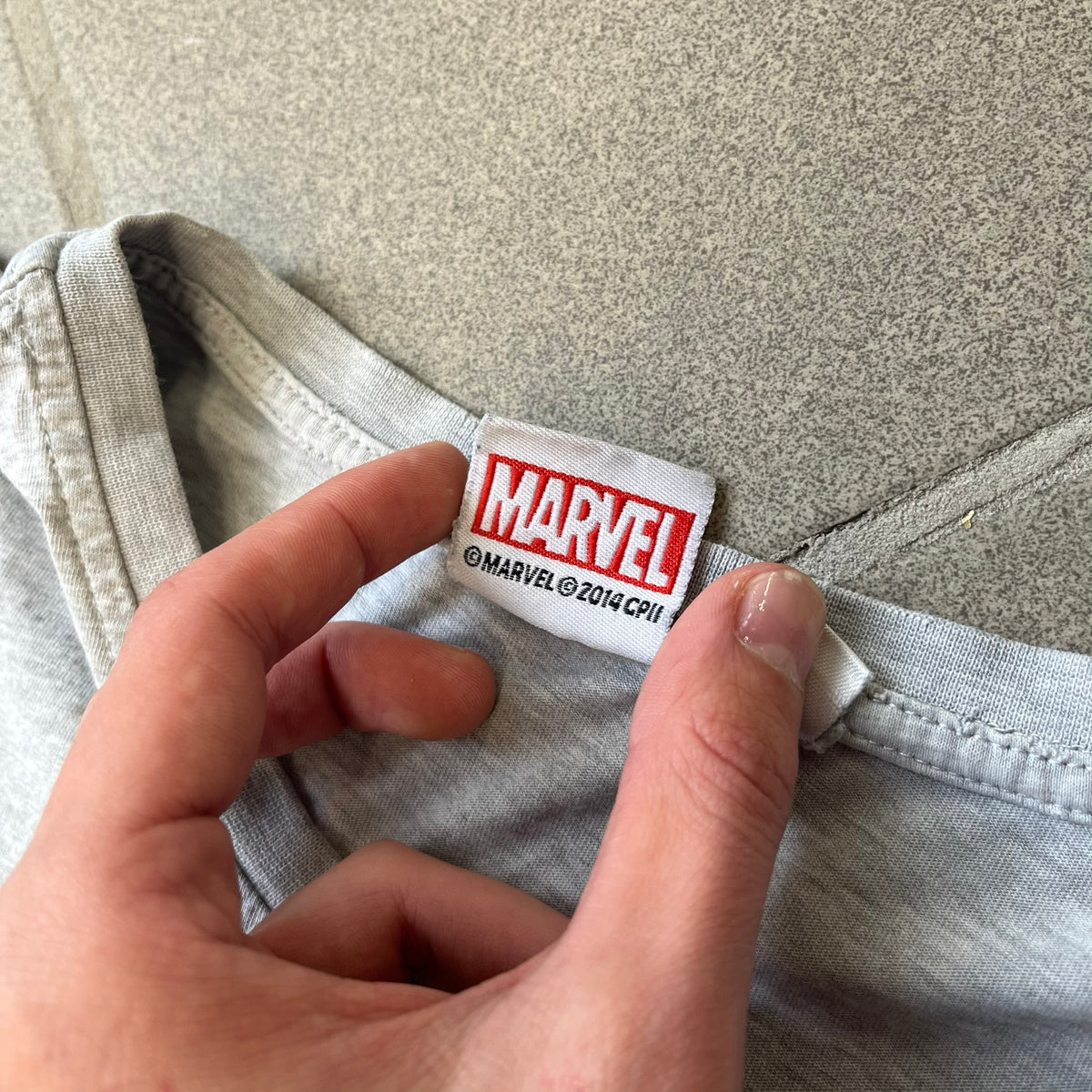 Gray 2014 Marvel tee featuring The Amazing Spider-Man 2 design with a “ripped page” effect showcasing Spider-Man’s face in the center. Text logo sits beneath the graphic for a bold cinematic touch. A collectible piece from the official movie merchandise line.