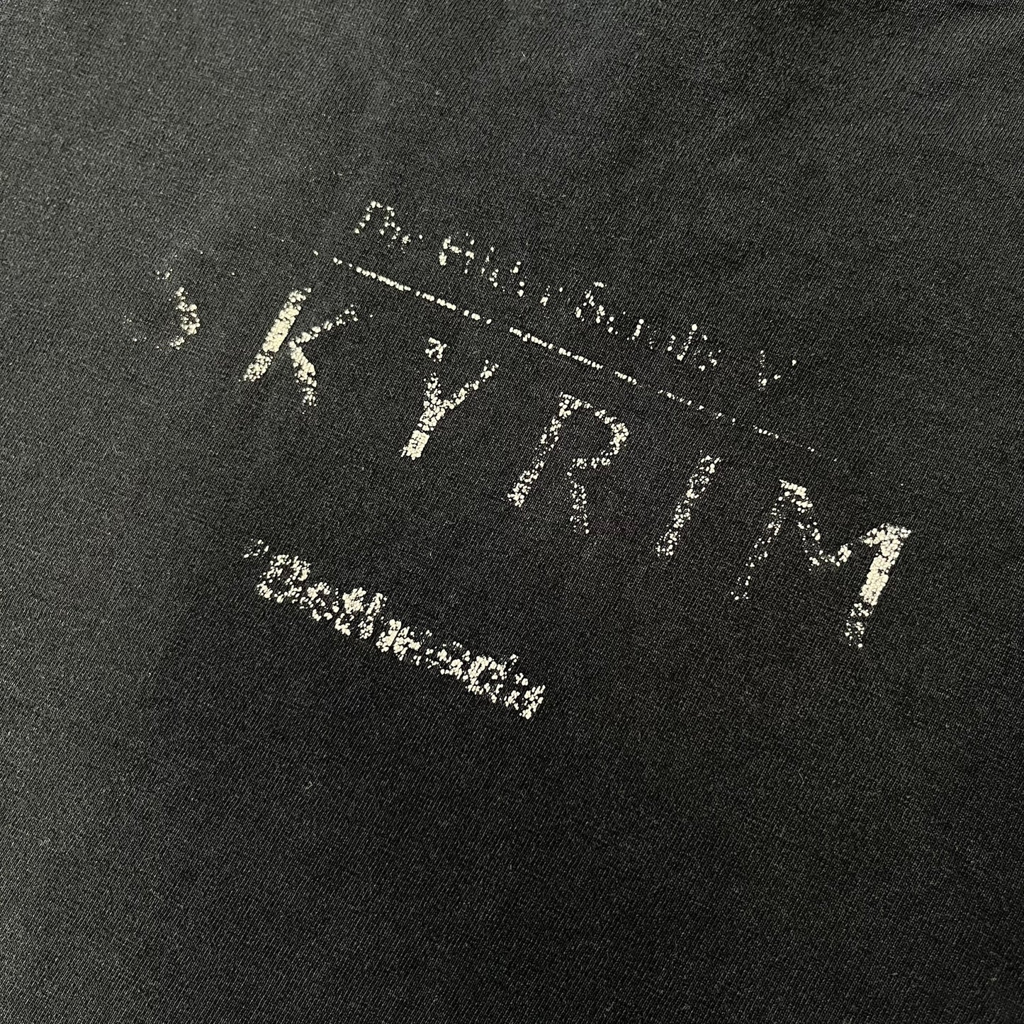 The Elder Scrolls V: Skyrim 2011 Promo Tee features a black design with the Skyrim dragon logo printed on the front chest. The upper back has the full “The Elder Scrolls V: Skyrim” text with Bethesda branding. Made on a Gildan blank.

