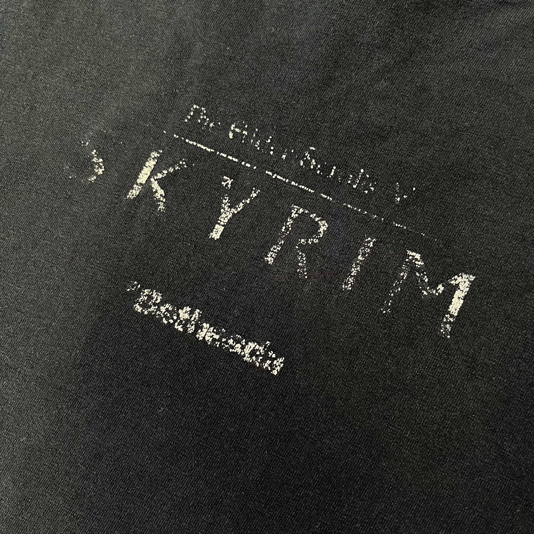The Elder Scrolls V: Skyrim 2011 Promo Tee features a black design with the Skyrim dragon logo printed on the front chest. The upper back has the full “The Elder Scrolls V: Skyrim” text with Bethesda branding. Made on a Gildan blank.
