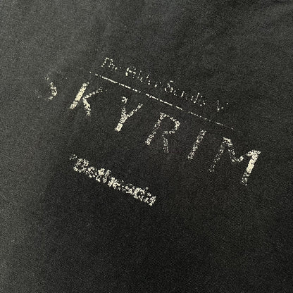 The Elder Scrolls V: Skyrim 2011 Promo Tee features a black design with the Skyrim dragon logo printed on the front chest. The upper back has the full “The Elder Scrolls V: Skyrim” text with Bethesda branding. Made on a Gildan blank.
