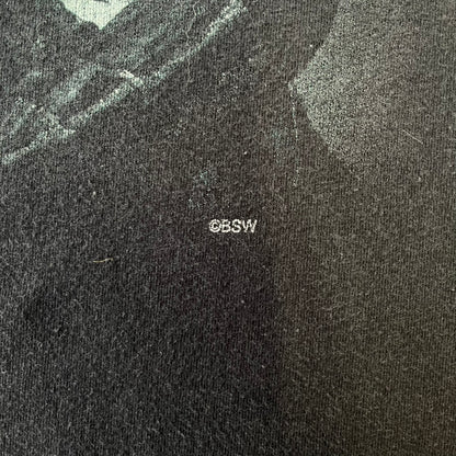 The Elder Scrolls V: Skyrim 2012 Dragonborn Tee features a black 100% cotton construction with the Dragonborn standing on top of a mountain, holding weapons and wearing a horned helmet. The Skyrim logo appears beside the character, with small white “@BSW” text underneath. Finished with a Bethesda licensed neck tag.
