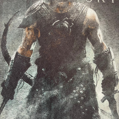 The Elder Scrolls V: Skyrim 2012 Dragonborn Tee features a black 100% cotton construction with the Dragonborn standing on top of a mountain, holding weapons and wearing a horned helmet. The Skyrim logo appears beside the character, with small white “@BSW” text underneath. Finished with a Bethesda licensed neck tag.
