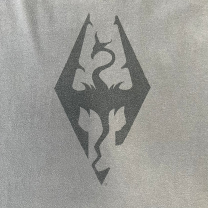 The Elder Scrolls V: Skyrim Premium Edition Tee comes from the 2012 Premium release of the game. Dark gray design with the Skyrim dragon logo printed on the front chest. The upper back has the full “The Elder Scrolls V: Skyrim” text. On the left sleeve there is a text in Dragon language. Made on a Gildan blank.
