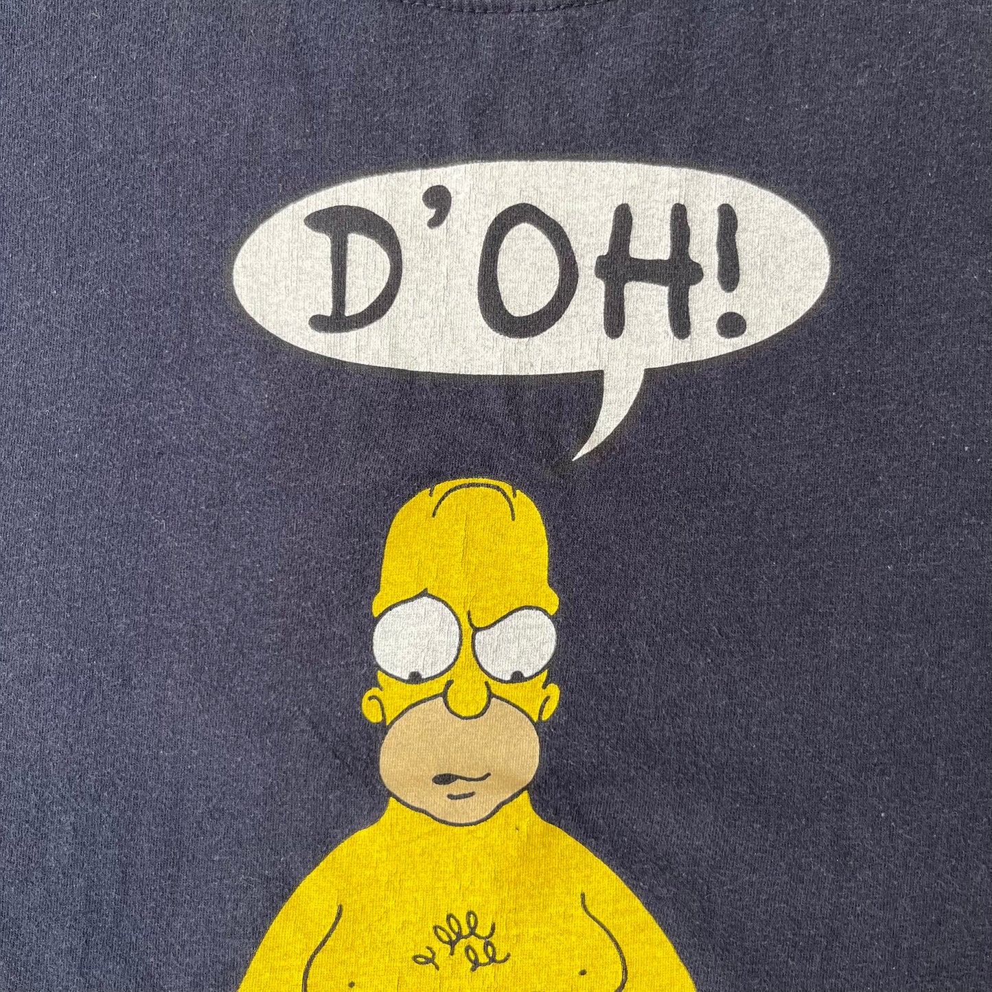 The Simpsons 1997 Homer “D’OH!” Black Tee features a black T-shirt with a front graphic of Homer Simpson standing in his underwear and looking down at a cracked scale while holding a chicken leg. A speech bubble above him reads “D’OH!”, with small Matt Groening 1997 licensing text underneath.
