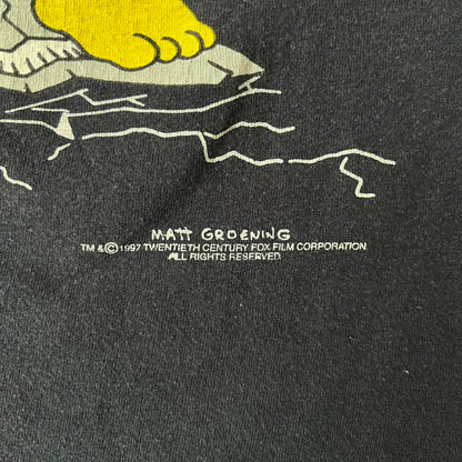 The Simpsons 1997 Homer “D’OH!” Black Tee features a black T-shirt with a front graphic of Homer Simpson standing in his underwear and looking down at a cracked scale while holding a chicken leg. A speech bubble above him reads “D’OH!”, with small Matt Groening 1997 licensing text underneath.
