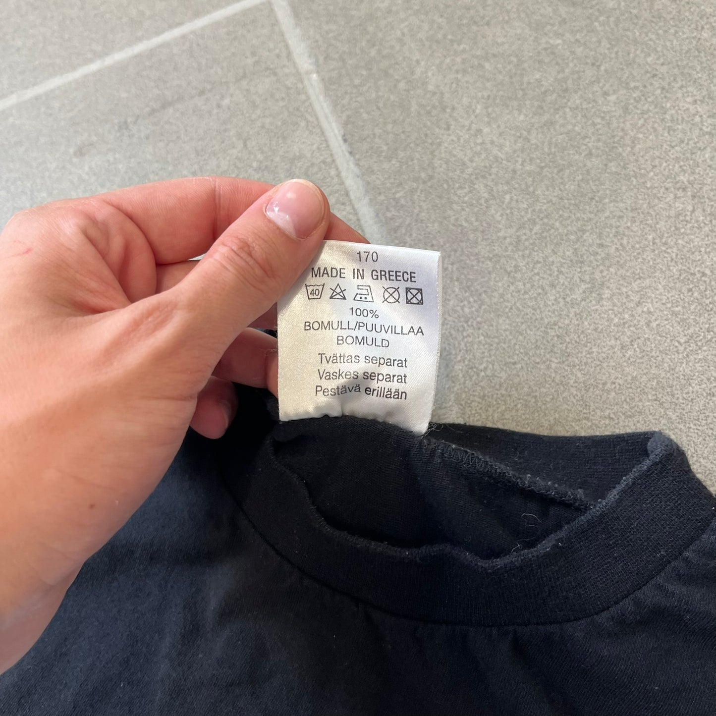 The Simpsons 1999 Bart Face Black Tee features a black T-shirt with a large front graphic of Bart Simpson’s face in black, grey, and white, showing a gritted-teeth expression. Small Matt Groening 1999 licensing text is printed below the graphic.
