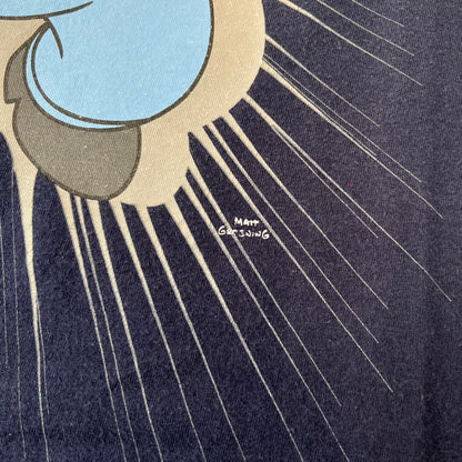 The Simpsons 2011 Angry Homer Navy Tee features a navy T-shirt with a front graphic of Homer Simpson running forward with an angry expression and reaching toward the viewer. The graphic has a grey glow-like background with small Matt Groening text beside Homer. Includes a 2011 licensed neck tag.
