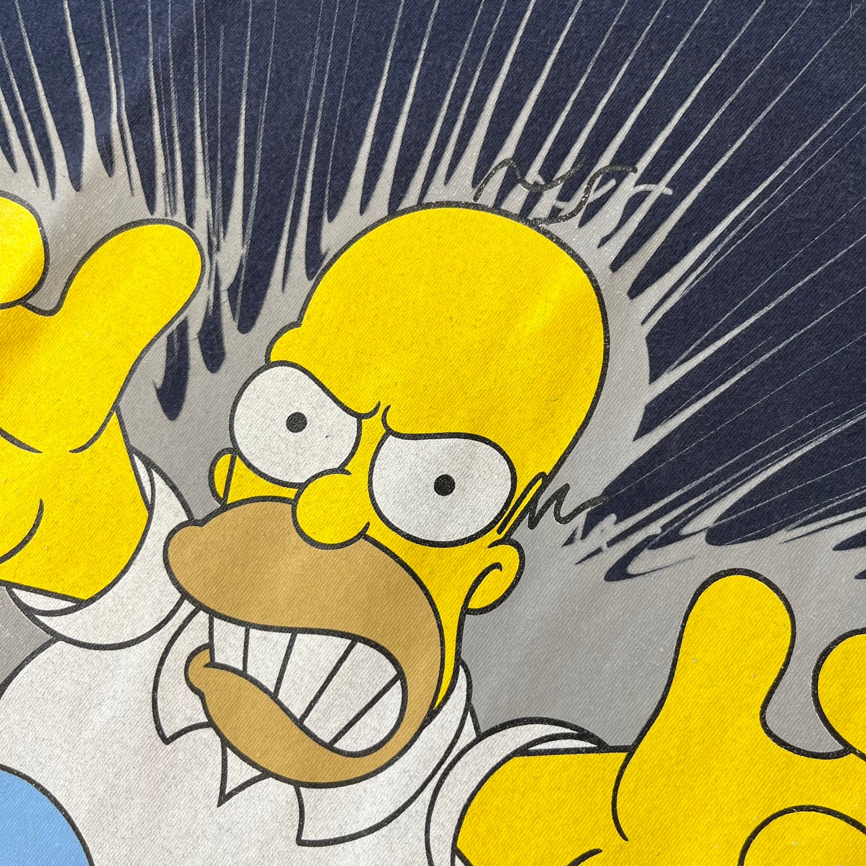 The Simpsons 2011 Angry Homer Navy Tee features a navy T-shirt with a front graphic of Homer Simpson running forward with an angry expression and reaching toward the viewer. The graphic has a grey glow-like background with small Matt Groening text beside Homer. Includes a 2011 licensed neck tag.
