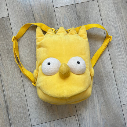 The Simpsons 1990's Bart Simpson Head Backpack is a novelty backpack shaped like a 3D Bart Simpson head. The design is fully yellow with soft sculpted facial features including eyes and nose, a molded mouth, and protruding hair. It includes yellow shoulder straps and a single main compartment.