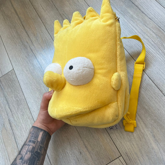 The Simpsons 1990's Bart Simpson Head Backpack is a novelty backpack shaped like a 3D Bart Simpson head. The design is fully yellow with soft sculpted facial features including eyes and nose, a molded mouth, and protruding hair. It includes yellow shoulder straps and a single main compartment.
