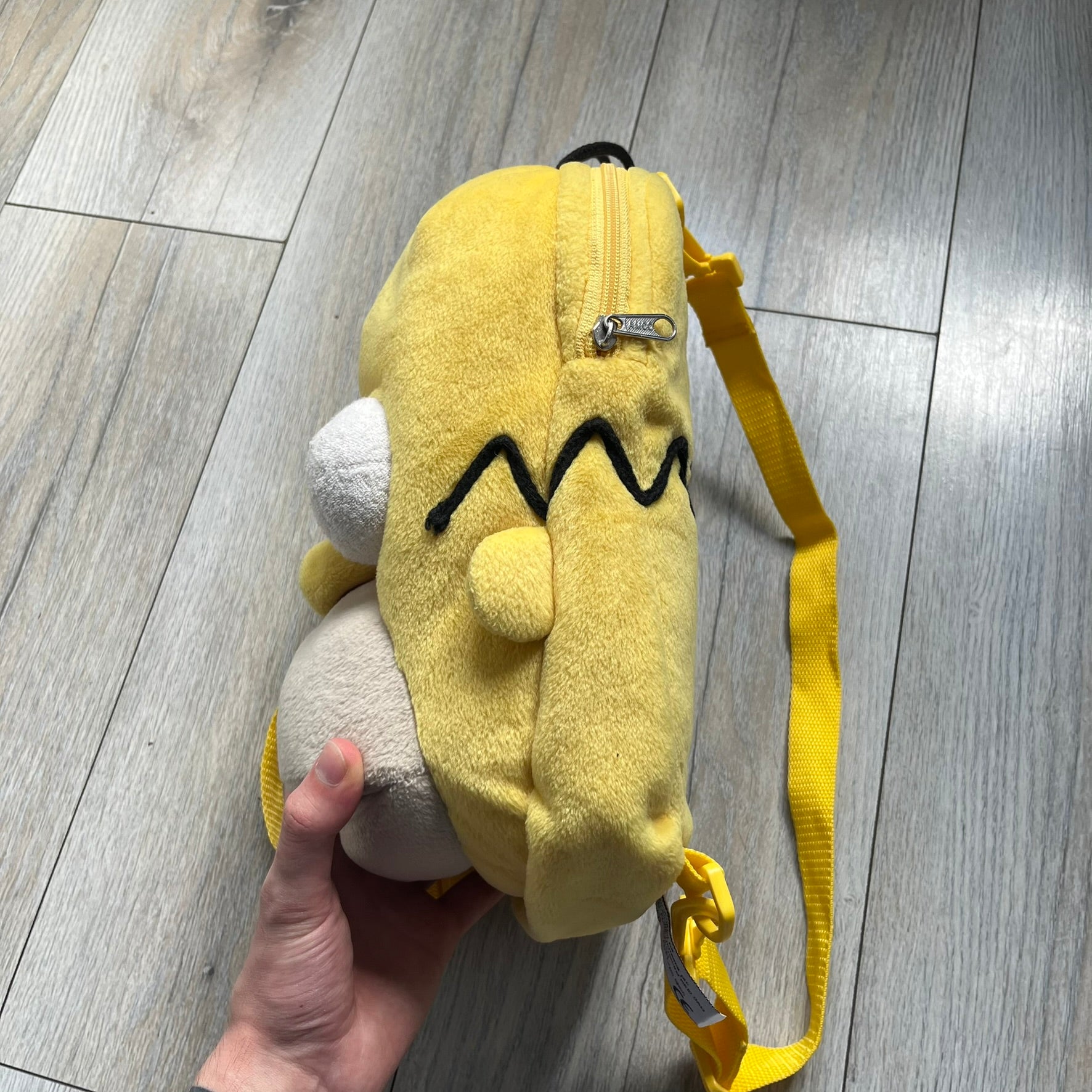 The Simpsons 1990s Homer Simpson Head Backpack is a novelty backpack shaped like a 3D Homer Simpson head. The design is fully yellow with soft sculpted facial features including eyes and nose, a molded mouth, and protruding ears. The hair detail wraps around the back, with the top strands functioning as a hanger. It includes yellow shoulder straps and a single main compartment.