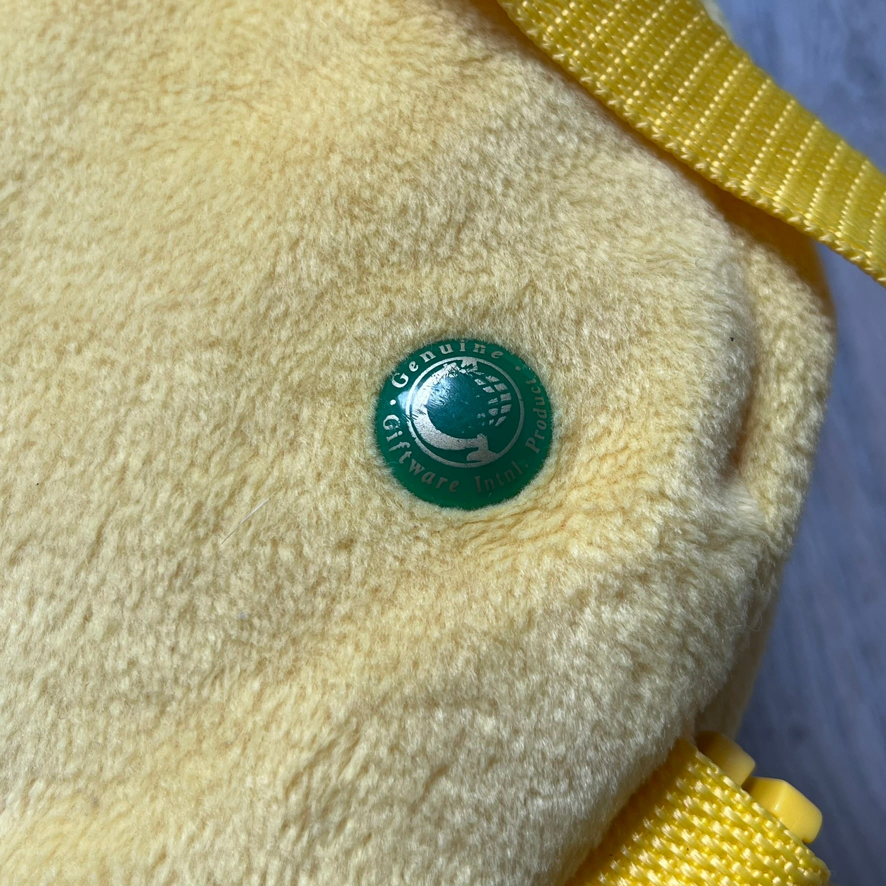 The Simpsons 1990s Homer Simpson Head Backpack is a novelty backpack shaped like a 3D Homer Simpson head. The design is fully yellow with soft sculpted facial features including eyes and nose, a molded mouth, and protruding ears. The hair detail wraps around the back, with the top strands functioning as a hanger. It includes yellow shoulder straps and a single main compartment.