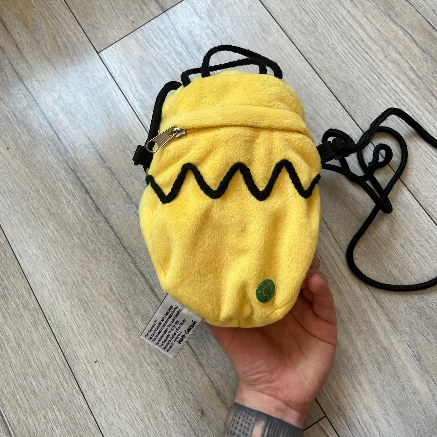 The Simpsons 1990s Homer Simpson Head Shoulder bag is shaped like a 3D Homer Simpson head. The design is yellow with soft sculpted facial features including eyes and nose, a molded beige mouth, and protruding ears. The hair detail wraps around the back, with the top strands functioning as a hanger. It includes a black string and a single main compartment.