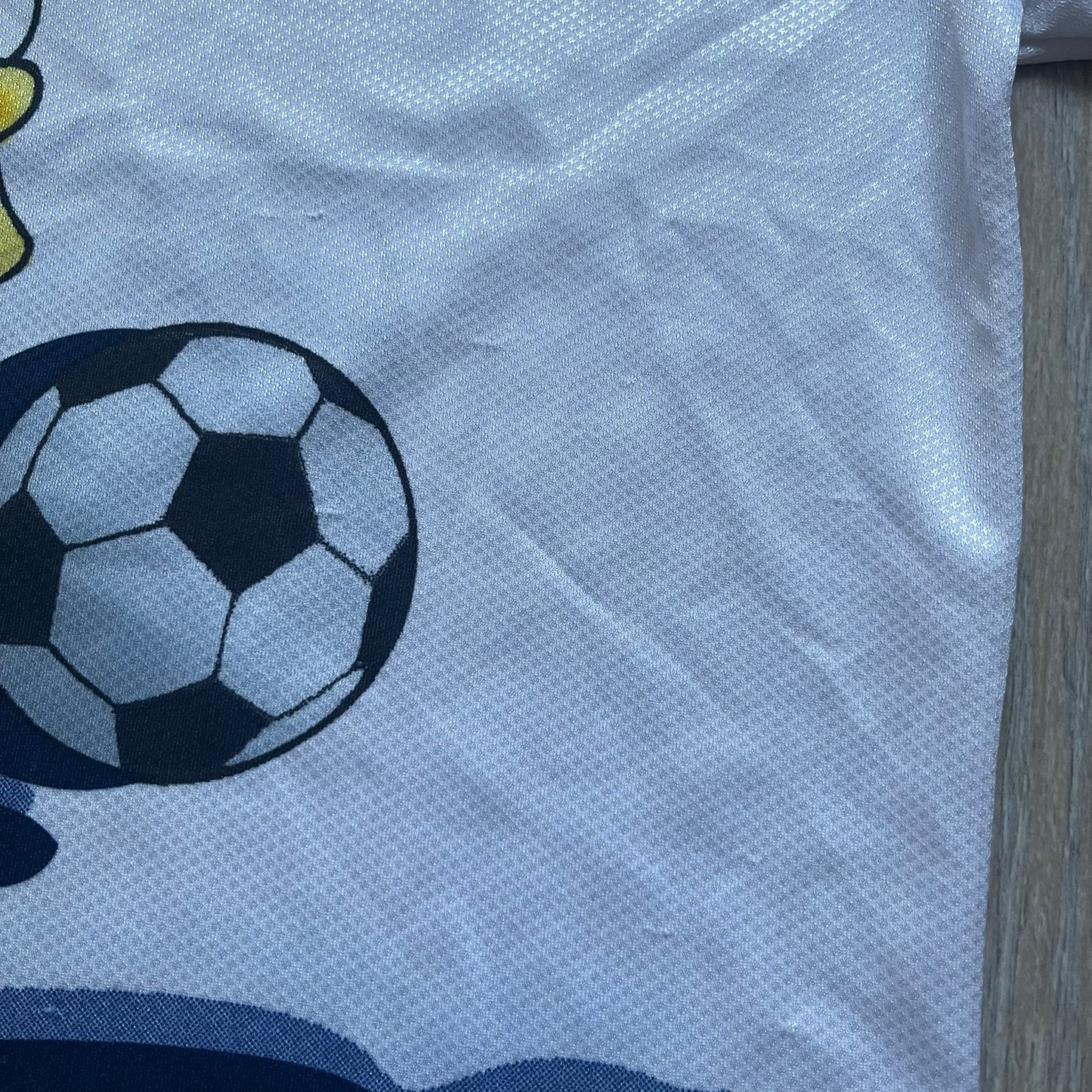 Officially licensed 1999 The Simpsons World Cup T-shirt for England. Lightweight white polyester tee featuring an all-over graphic design. The front shows Bart Simpson kicking a football, dressed in a white tee, with multiple England three-lions emblems layered across the background from top to bottom. Red “Bart” text details appear on the sleeve hems, with Matt Groening / The Simpsons ©1999 licensing printed beneath the main graphic.&nbsp;The back mirrors the artwork in a flipped layout, showing Bart from 