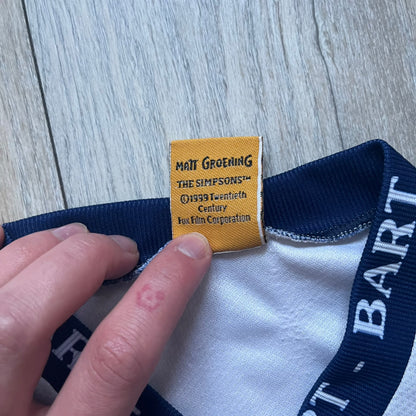 Officially licensed 1999 The Simpsons World Cup T-shirt for England. Lightweight white polyester tee featuring an all-over graphic design. The front shows Bart Simpson kicking a football, dressed in a white tee, with multiple England three-lions emblems layered across the background from top to bottom. Red “Bart” text details appear on the sleeve hems, with Matt Groening / The Simpsons ©1999 licensing printed beneath the main graphic.&nbsp;The back mirrors the artwork in a flipped layout, showing Bart from 