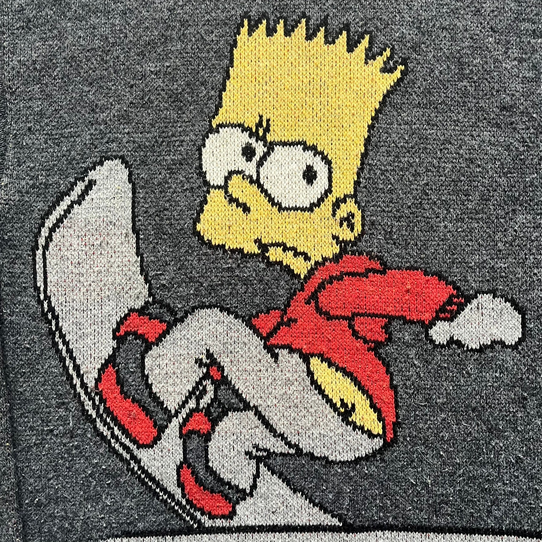 The Simpsons “Bart Freestyle” 2003 Knit Sweater is a gray knit featuring a large woven graphic of Bart snowboarding on the front, with “Bart” text placed below the character. On the back, in the same position as the front graphic, there is “Freestyle” text.&nbsp;It includes a Matt Groening The Simpsons 2003 FOX neck tag.