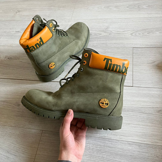 Timberland 6-Inch x Zoolander Olive Boots, model A1QTY / A2040. These collaboration boots feature an olive/army green upper with an orange metal Timberland logo on the side and an orange padded collar with large olive Timberland text. The laces are olive with small orange speckled details, matched by orange lace eyelets. This Zoolander collaboration was not sold in the United States and is considered extremely difficult to find.