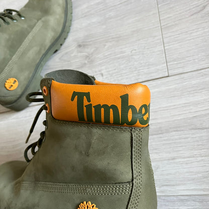 Timberland 6-Inch x Zoolander Olive Boots, model A1QTY / A2040. These collaboration boots feature an olive/army green upper with an orange metal Timberland logo on the side and an orange padded collar with large olive Timberland text. The laces are olive with small orange speckled details, matched by orange lace eyelets. This Zoolander collaboration was not sold in the United States and is considered extremely difficult to find.