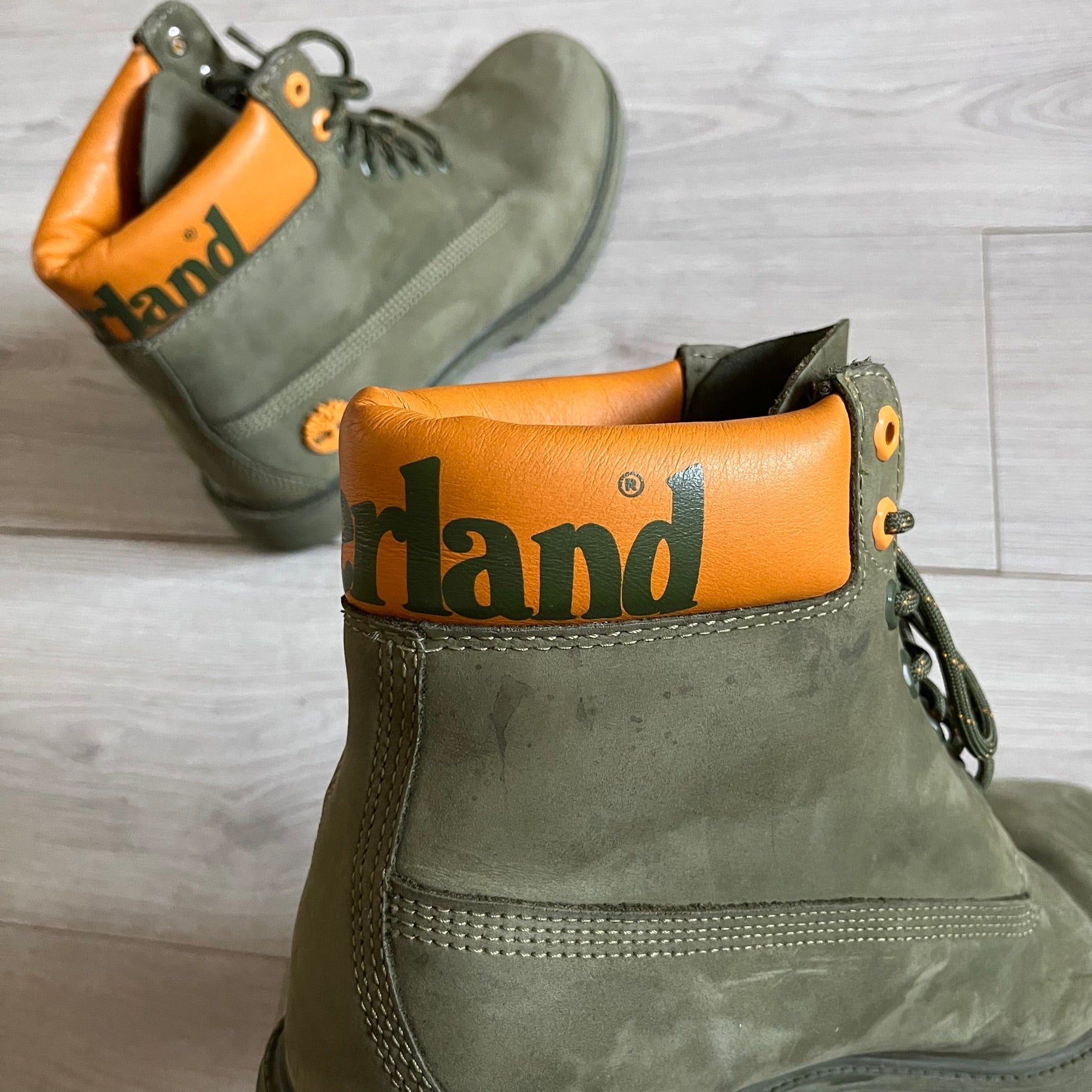 Timberland 6-Inch x Zoolander Olive Boots, model A1QTY / A2040. These collaboration boots feature an olive/army green upper with an orange metal Timberland logo on the side and an orange padded collar with large olive Timberland text. The laces are olive with small orange speckled details, matched by orange lace eyelets. This Zoolander collaboration was not sold in the United States and is considered extremely difficult to find.