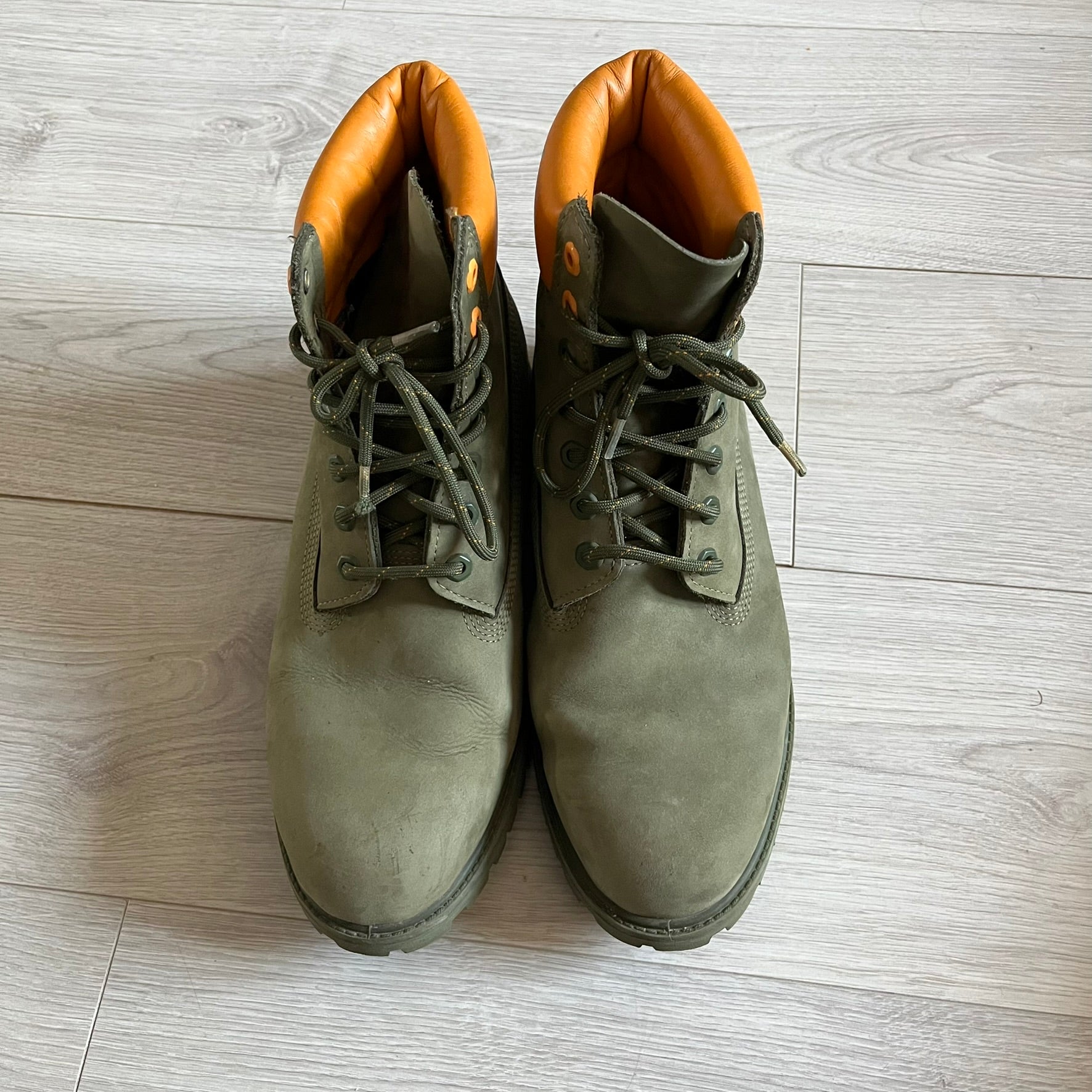 Timberland 6-Inch x Zoolander Olive Boots, model A1QTY / A2040. These collaboration boots feature an olive/army green upper with an orange metal Timberland logo on the side and an orange padded collar with large olive Timberland text. The laces are olive with small orange speckled details, matched by orange lace eyelets. This Zoolander collaboration was not sold in the United States and is considered extremely difficult to find.