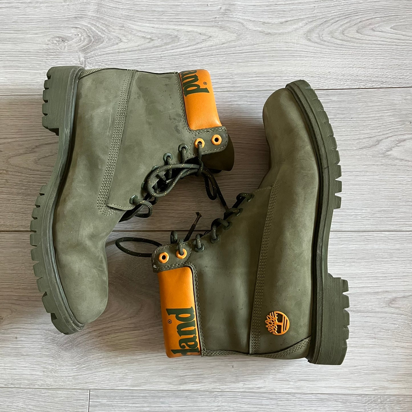 Timberland 6-Inch x Zoolander Olive Boots, model A1QTY / A2040. These collaboration boots feature an olive/army green upper with an orange metal Timberland logo on the side and an orange padded collar with large olive Timberland text. The laces are olive with small orange speckled details, matched by orange lace eyelets. This Zoolander collaboration was not sold in the United States and is considered extremely difficult to find.