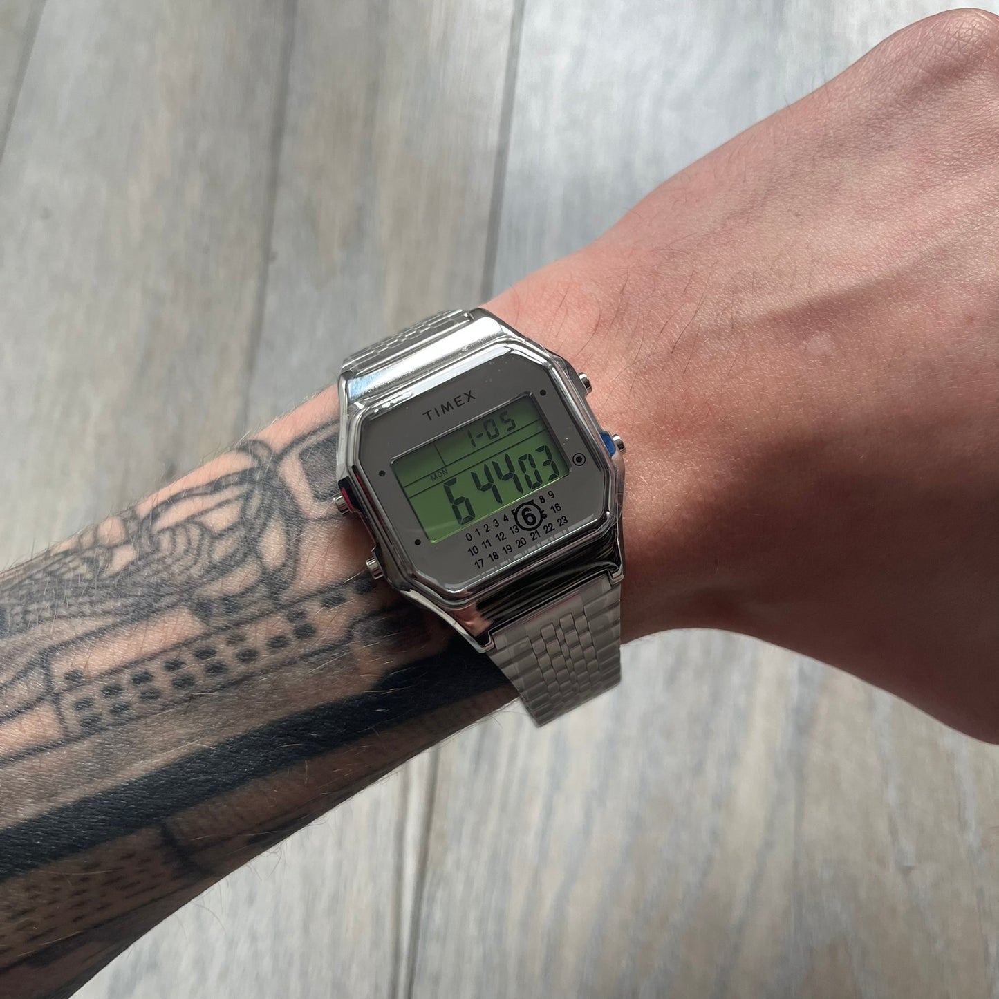 Timex x Maison Margiela MM6 Gift Set TWG065600 is a collaborative reinterpretation of the classic Timex T80, released on October 24, 2024. Crafted from polished and brushed stainless steel, it features a 36mm digital case with Timex branding and a distinctive 0–23 numeral layout, including a subtle circled “6” nod to MM6 design language. The watch offers 100 ft water resistance, mineral glass, backlight, alarm, timer, and date functions, and is presented as a 2-in-1 gift set with an additional standalone st