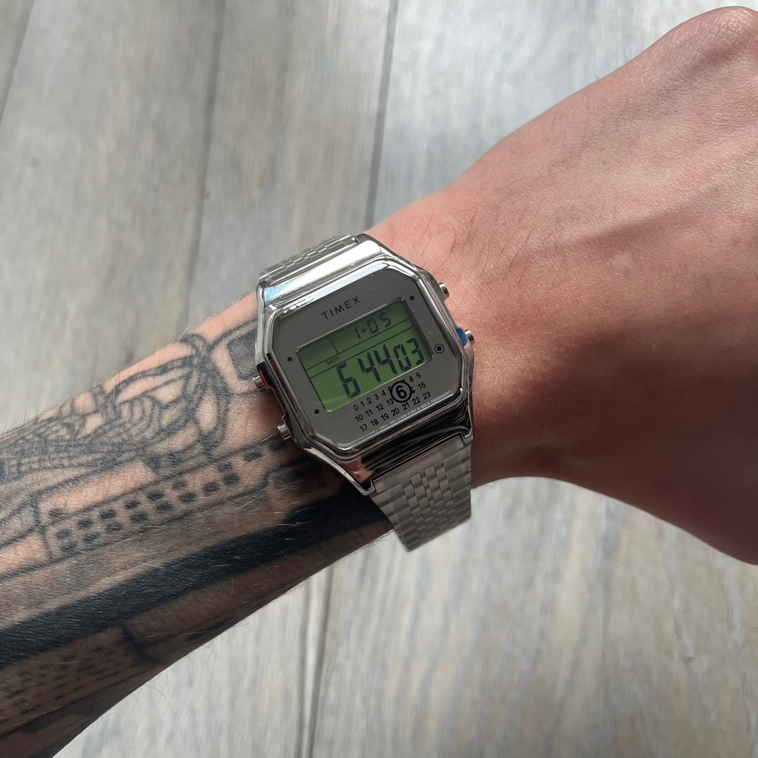 Timex x Maison Margiela MM6 Gift Set TWG065600 is a collaborative reinterpretation of the classic Timex T80, released on October 24, 2024. Crafted from polished and brushed stainless steel, it features a 36mm digital case with Timex branding and a distinctive 0–23 numeral layout, including a subtle circled “6” nod to MM6 design language. The watch offers 100 ft water resistance, mineral glass, backlight, alarm, timer, and date functions, and is presented as a 2-in-1 gift set with an additional standalone st