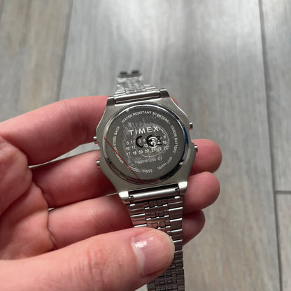Timex x Maison Margiela MM6 Gift Set TWG065600 is a collaborative reinterpretation of the classic Timex T80, released on October 24, 2024. Crafted from polished and brushed stainless steel, it features a 36mm digital case with Timex branding and a distinctive 0–23 numeral layout, including a subtle circled “6” nod to MM6 design language. The watch offers 100 ft water resistance, mineral glass, backlight, alarm, timer, and date functions, and is presented as a 2-in-1 gift set with an additional standalone st