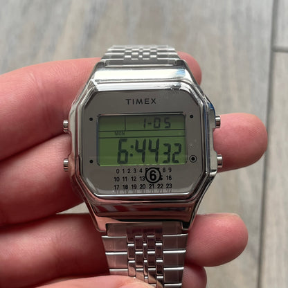 Timex x Maison Margiela MM6 Gift Set TWG065600 is a collaborative reinterpretation of the classic Timex T80, released on October 24, 2024. Crafted from polished and brushed stainless steel, it features a 36mm digital case with Timex branding and a distinctive 0–23 numeral layout, including a subtle circled “6” nod to MM6 design language. The watch offers 100 ft water resistance, mineral glass, backlight, alarm, timer, and date functions, and is presented as a 2-in-1 gift set with an additional standalone st