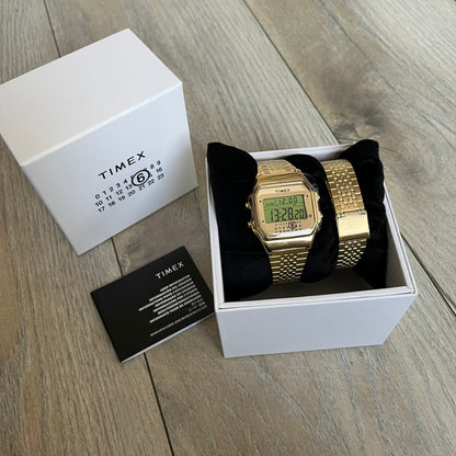 Timex x Maison Margiela MM6 Gold Watch + Bracelet Gift Set TWG067500QY is a collaborative reinterpretation of the classic Timex T80, released on October 24, 2024. Crafted from polished and brushed stainless steel, it features a 36mm digital case with Timex branding and a distinctive 0–23 numeral layout, including a subtle circled “6” nod to MM6 design language. The watch offers 100 ft water resistance, mineral glass, backlight, alarm, timer, and date functions, and is presented as a 2-in-1 gift set with an 