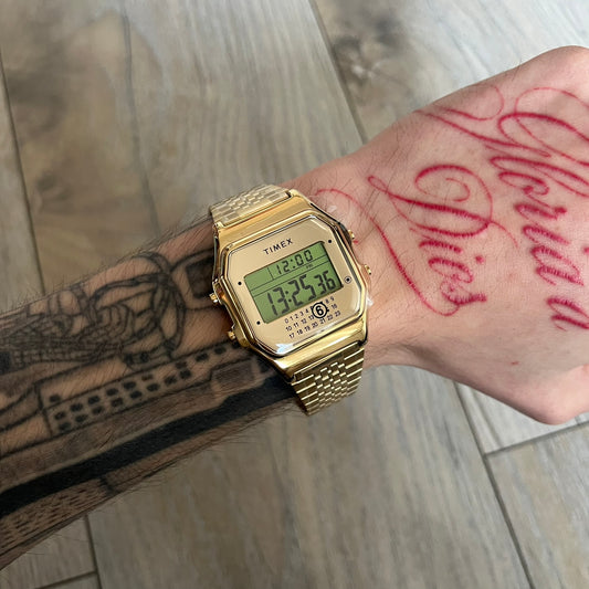 Timex x Maison Margiela MM6 Gold Watch + Bracelet Gift Set TWG067500QY is a collaborative reinterpretation of the classic Timex T80, released on October 24, 2024. Crafted from polished and brushed stainless steel, it features a 36mm digital case with Timex branding and a distinctive 0–23 numeral layout, including a subtle circled “6” nod to MM6 design language. The watch offers 100 ft water resistance, mineral glass, backlight, alarm, timer, and date functions, and is presented as a 2-in-1 gift set with an 
