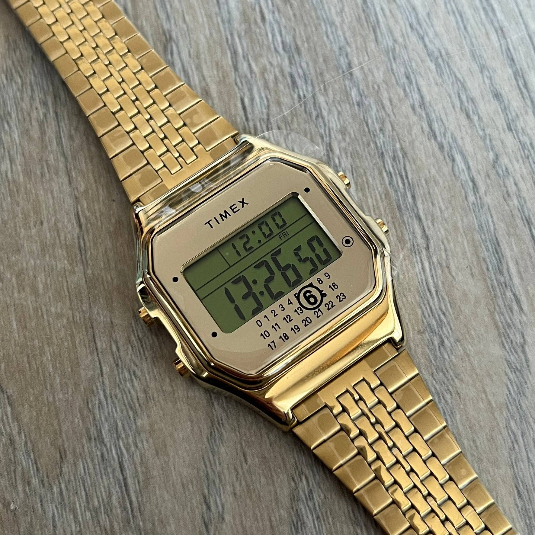 Timex x Maison Margiela MM6 Gold Watch + Bracelet Gift Set TWG067500QY is a collaborative reinterpretation of the classic Timex T80, released on October 24, 2024. Crafted from polished and brushed stainless steel, it features a 36mm digital case with Timex branding and a distinctive 0–23 numeral layout, including a subtle circled “6” nod to MM6 design language. The watch offers 100 ft water resistance, mineral glass, backlight, alarm, timer, and date functions, and is presented as a 2-in-1 gift set with an 