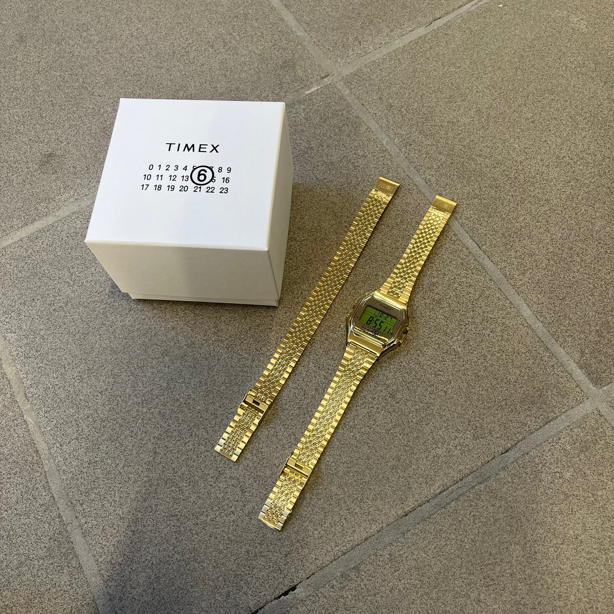 Timex x Maison Margiela MM6 Gold Watch + Bracelet Gift Set TWG067500QY is a collaborative reinterpretation of the classic Timex T80, released on October 24, 2024. Crafted from polished and brushed stainless steel, it features a 36mm digital case with Timex branding and a distinctive 0–23 numeral layout, including a subtle circled “6” nod to MM6 design language. The watch offers 100 ft water resistance, mineral glass, backlight, alarm, timer, and date functions, and is presented as a 2-in-1 gift set with an 