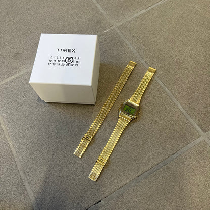 Timex x Maison Margiela MM6 Gold Watch + Bracelet Gift Set TWG067500QY is a collaborative reinterpretation of the classic Timex T80, released on October 24, 2024. Crafted from polished and brushed stainless steel, it features a 36mm digital case with Timex branding and a distinctive 0–23 numeral layout, including a subtle circled “6” nod to MM6 design language. The watch offers 100 ft water resistance, mineral glass, backlight, alarm, timer, and date functions, and is presented as a 2-in-1 gift set with an 