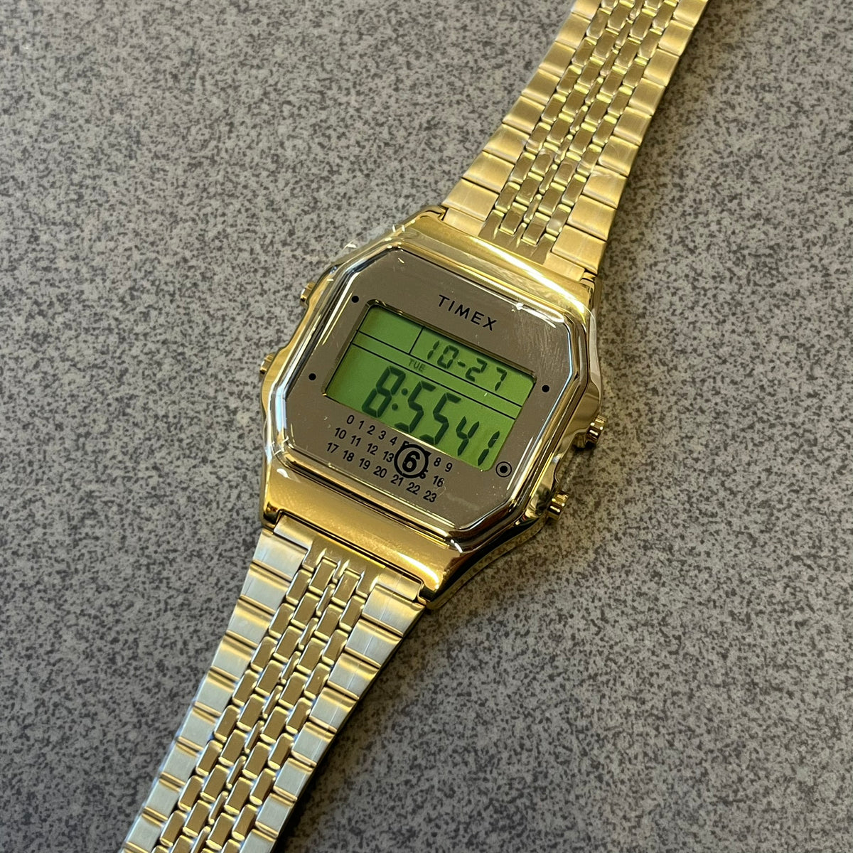 Timex x Maison Margiela MM6 Gold Watch + Bracelet Gift Set TWG067500QY is a collaborative reinterpretation of the classic Timex T80, released on October 24, 2024. Crafted from polished and brushed stainless steel, it features a 36mm digital case with Timex branding and a distinctive 0–23 numeral layout, including a subtle circled “6” nod to MM6 design language. The watch offers 100 ft water resistance, mineral glass, backlight, alarm, timer, and date functions, and is presented as a 2-in-1 gift set with an 