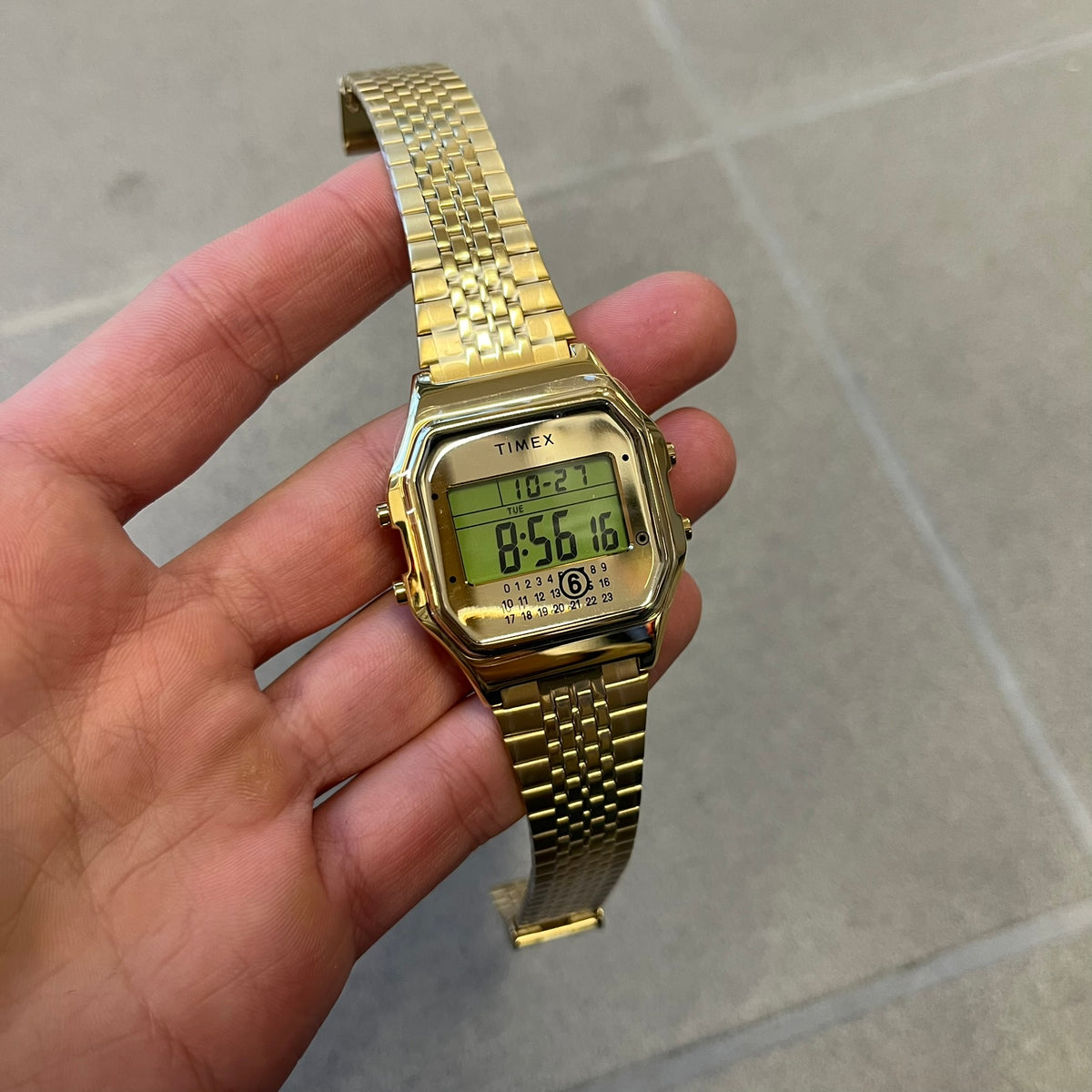 Timex x Maison Margiela MM6 Gold Watch + Bracelet Gift Set TWG067500QY is a collaborative reinterpretation of the classic Timex T80, released on October 24, 2024. Crafted from polished and brushed stainless steel, it features a 36mm digital case with Timex branding and a distinctive 0–23 numeral layout, including a subtle circled “6” nod to MM6 design language. The watch offers 100 ft water resistance, mineral glass, backlight, alarm, timer, and date functions, and is presented as a 2-in-1 gift set with an 