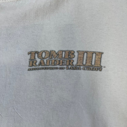 Tomb Raider III 1998 “Lara’s Back” White Tee is a boxy white T-shirt made on a Sierra Teez blank, with a stone-styled Tomb Raider III: Adventures of Lara Croft logo on the front. The back has a low-poly graphic of Lara Croft ass with “Lara’s Back...” text underneath, and the sleeve carries Eidos and Core logos.